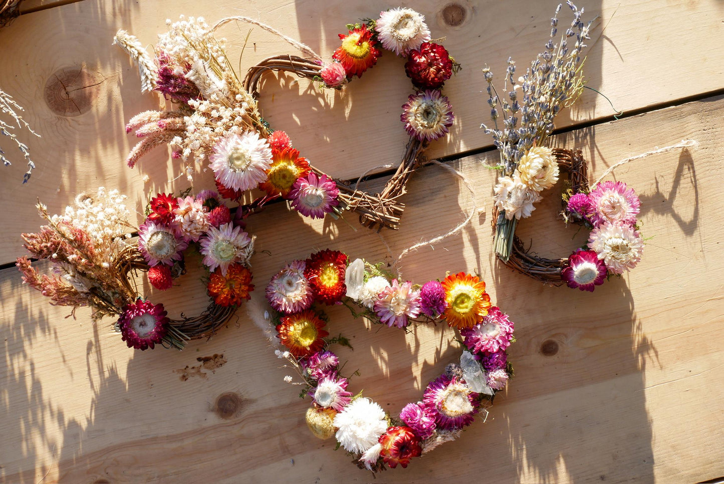 a collection of wreaths made from dried flowers and twigs, arranged on a wooden surface.
