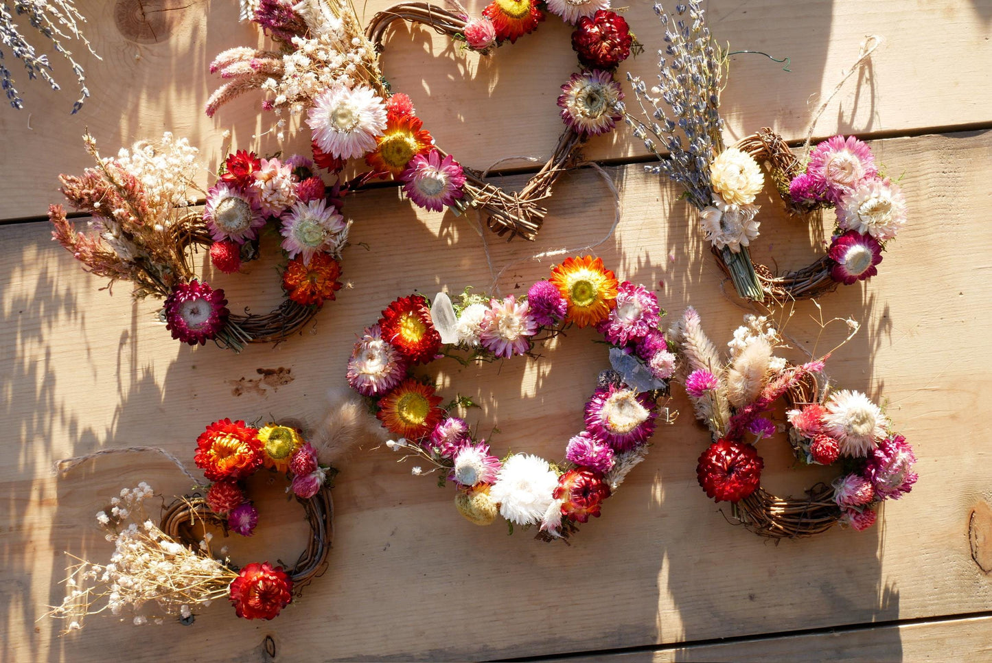 a collection of heart-shaped wreaths made from dried flowers, arranged on a wooden surface.