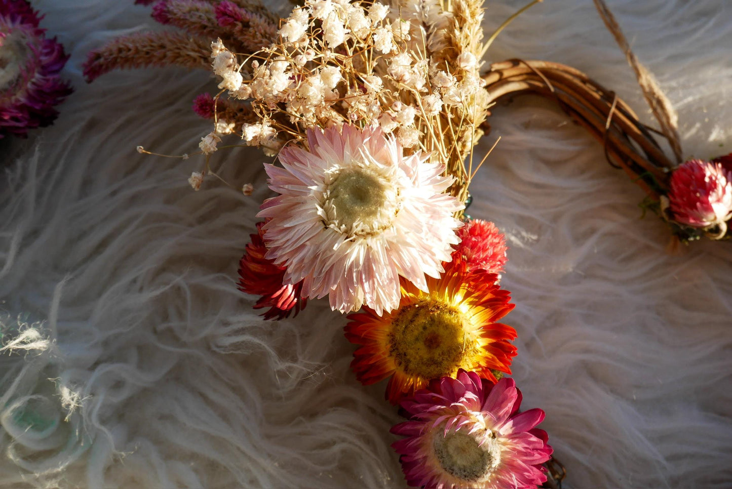 A bouquet of dried flowers and colorful flowers arranged on a white furry surface.