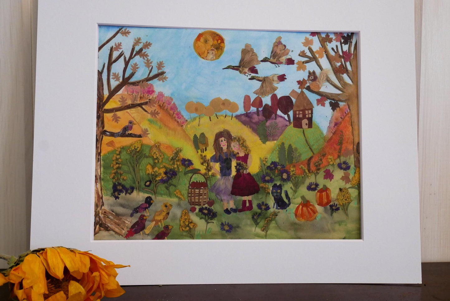 The image is a vibrant, hand-painted collage depicting a lively autumn scene with a woman, children, birds, and various fall-themed elements.