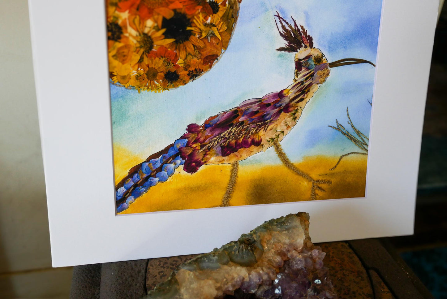 The image is a vibrant painting of a colorful bird, possibly a roadrunner, set against a backdrop of a sunflower and a desert landscape.