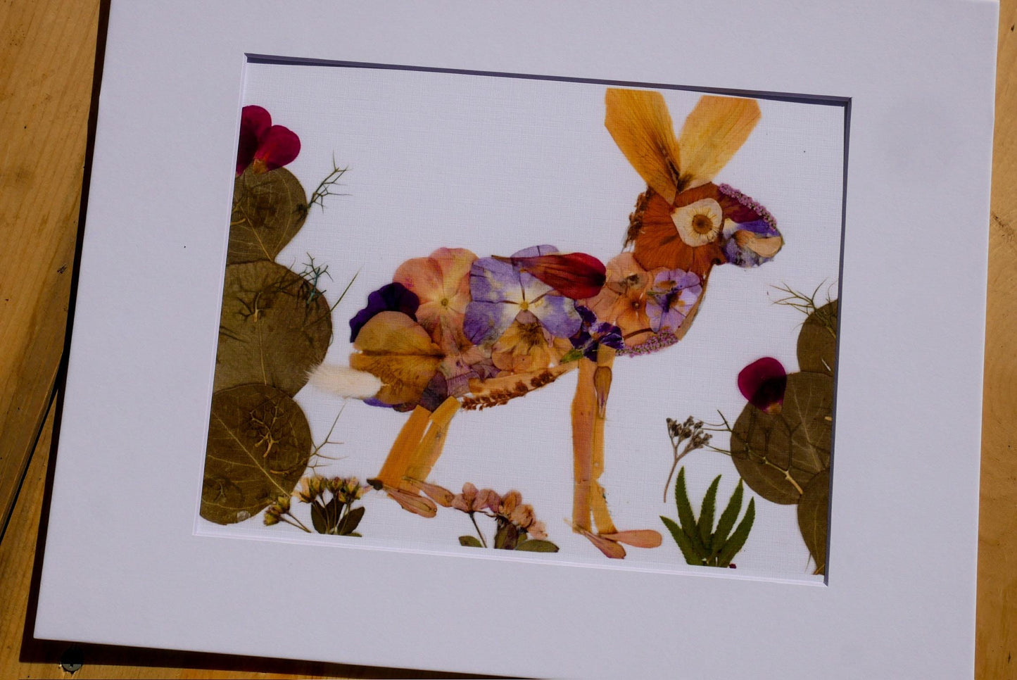 A framed artwork depicting a colorful rabbit made of dried flowers and leaves, set against a natural background.