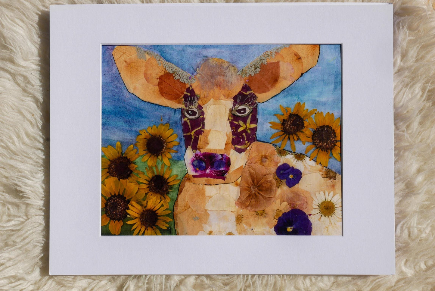 The image is a collage featuring a cow surrounded by a variety of colorful flowers, including sunflowers and daisies.