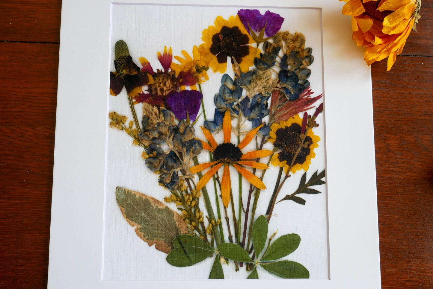 A framed arrangement of dried flowers and leaves, showcasing a vibrant and colorful floral display.
