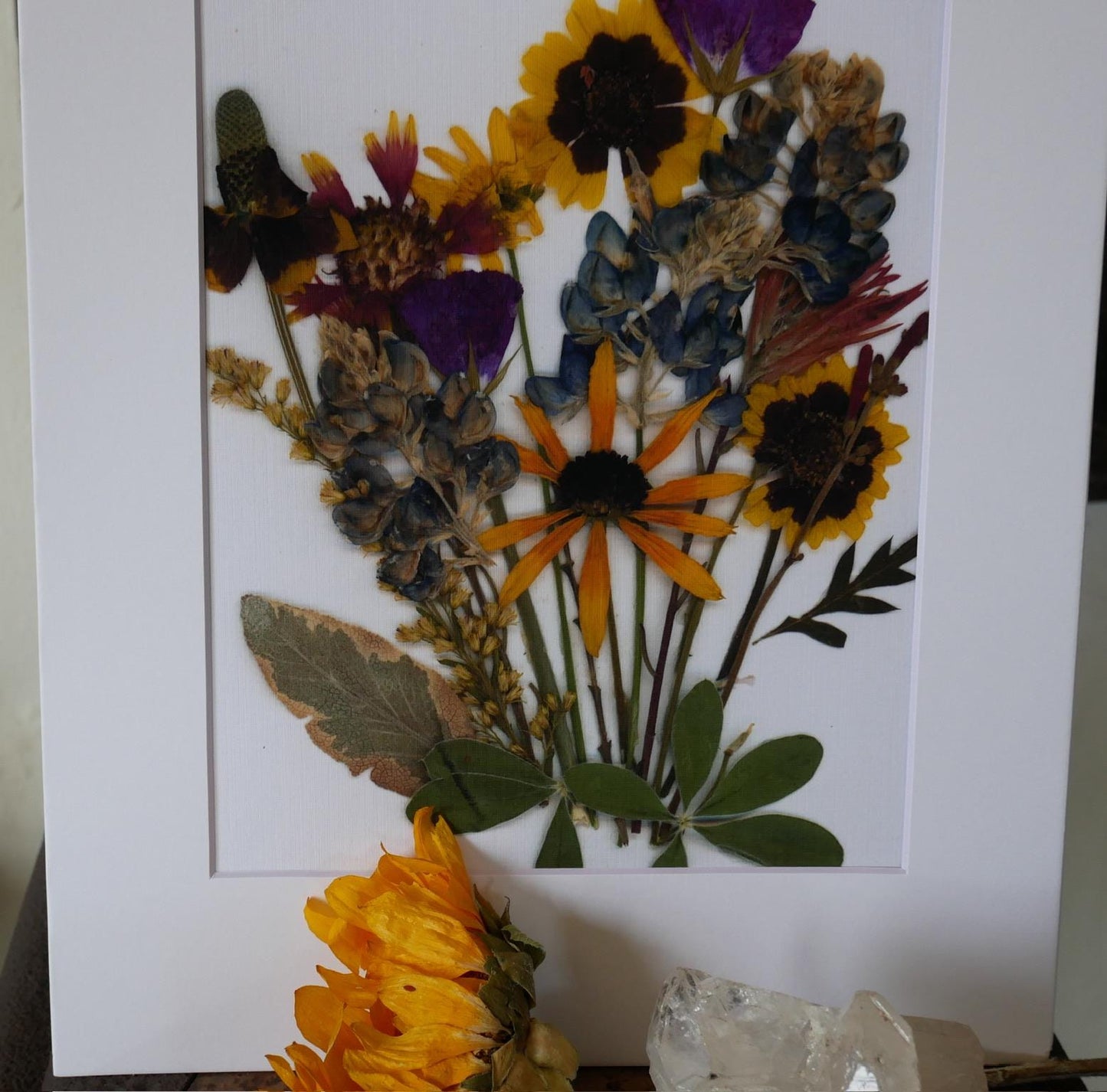 a vibrant bouquet of dried flowers, including sunflowers, daisies, and other colorful blooms, arranged in a white frame.