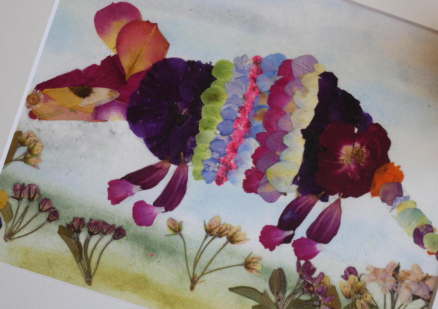 A collage of various colorful flower petals and leaves arranged to form the shape of a small animal, such as a cat or a rabbit.