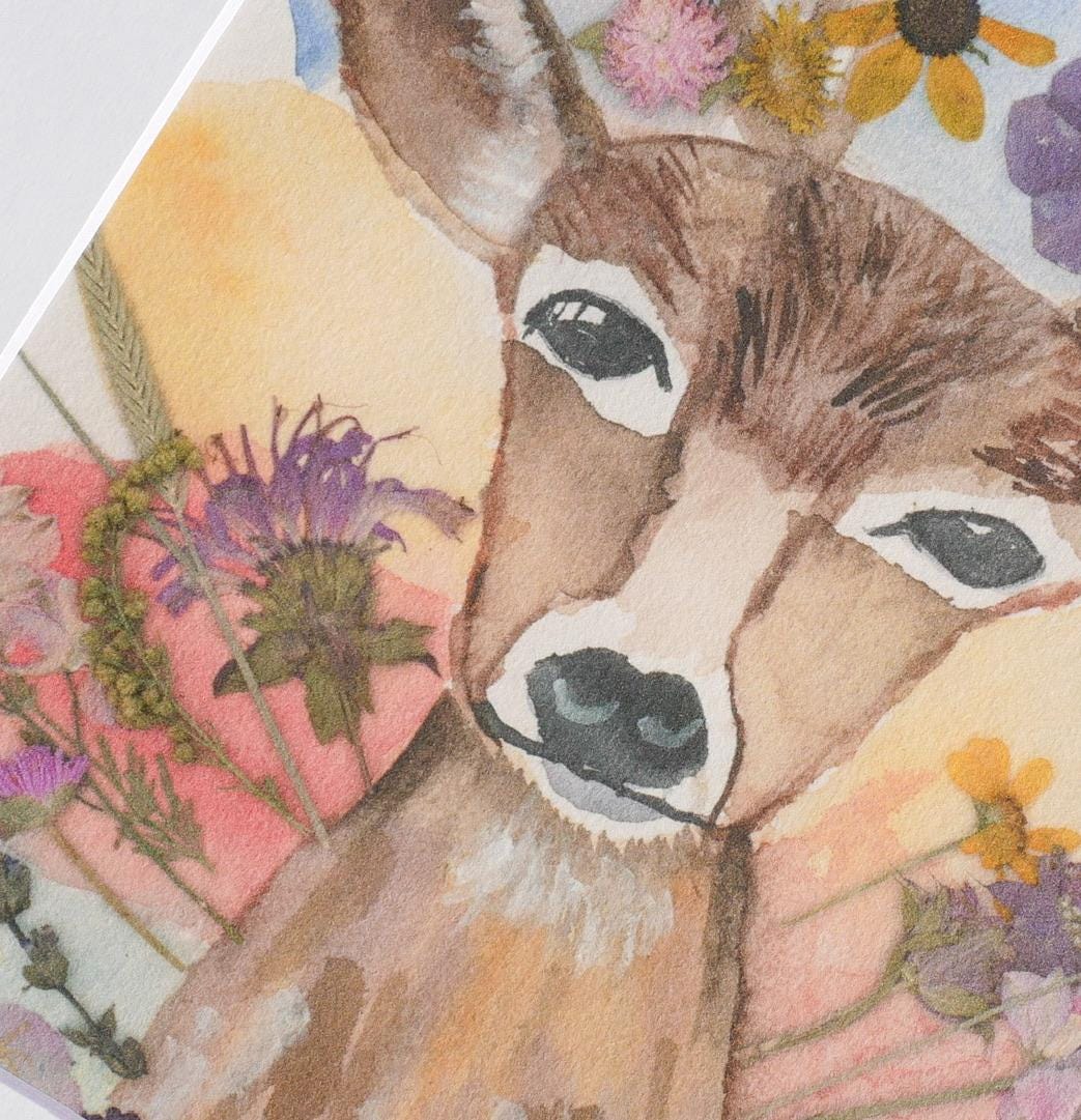 A watercolor painting of a deer with large eyes and a black nose, surrounded by colorful flowers and foliage.