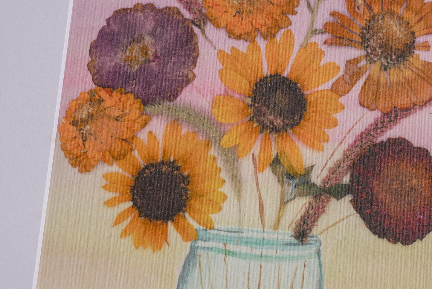 A close-up of a vase filled with vibrant yellow sunflowers and purple flowers against a pink background.