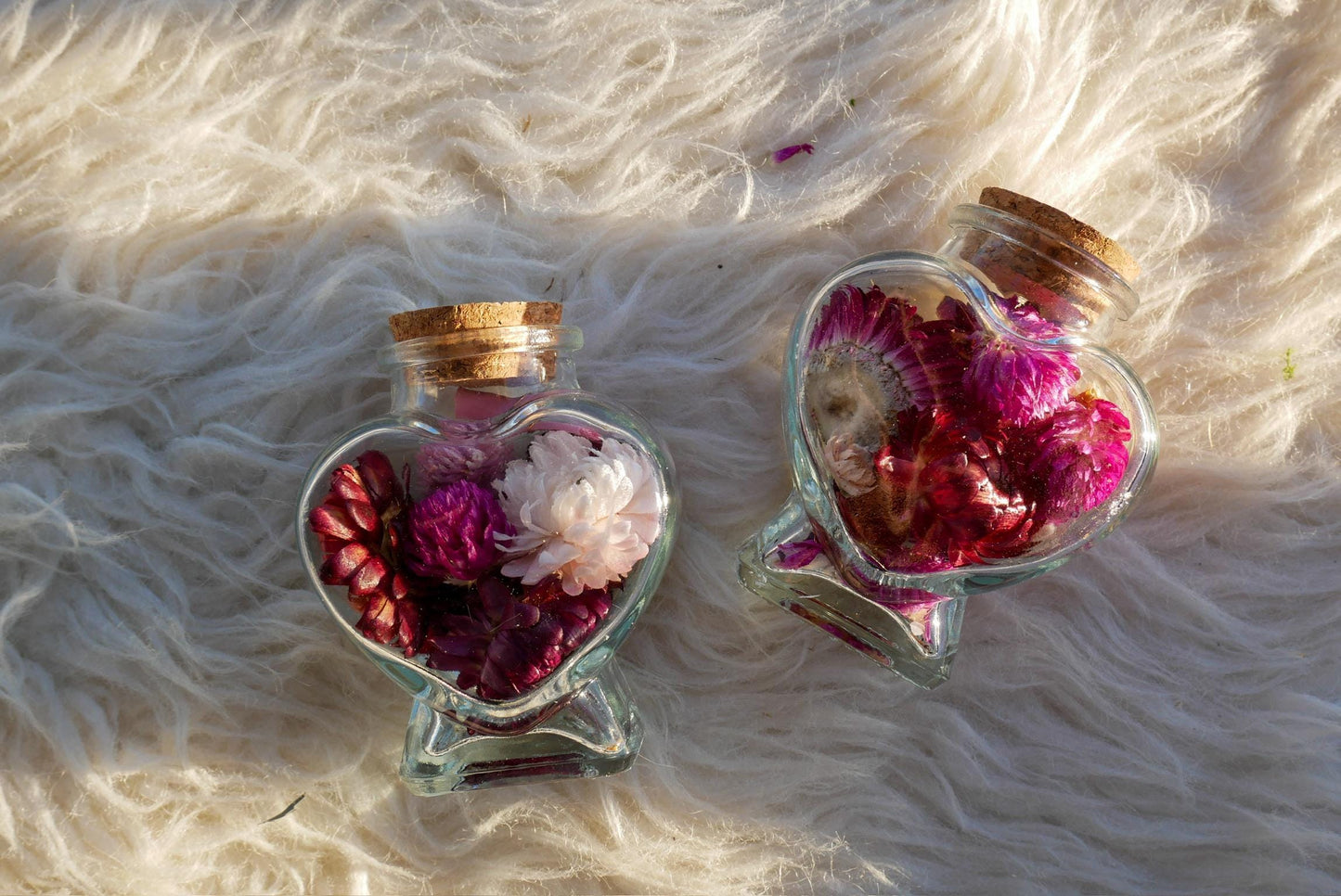 Two glass bottles filled with colorful flowers, including pink and white flowers, placed on a white furry surface.