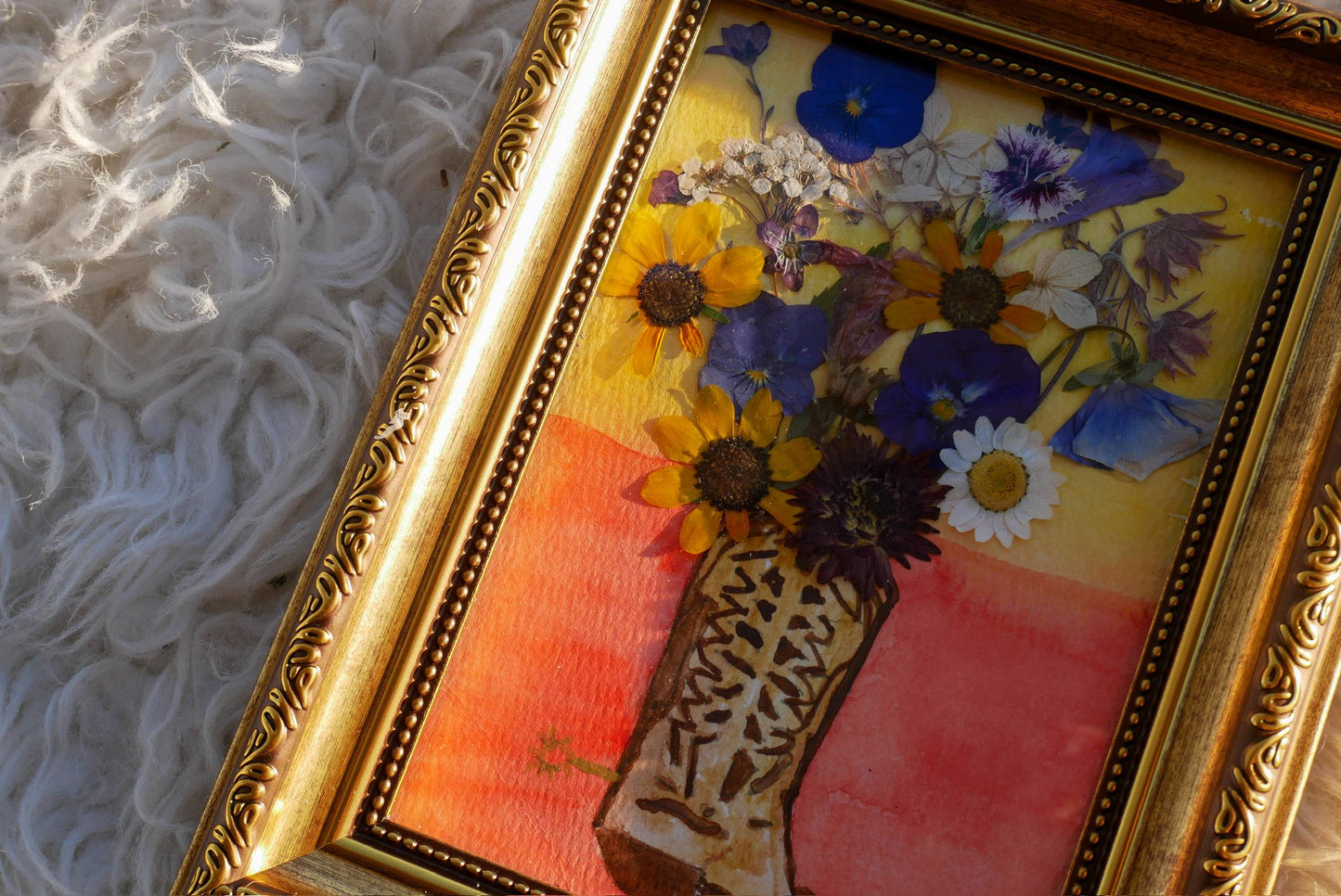 A framed painting depicting a vase filled with a variety of colorful flowers, including sunflowers, daisies, and other blooms, set against a vibrant background.